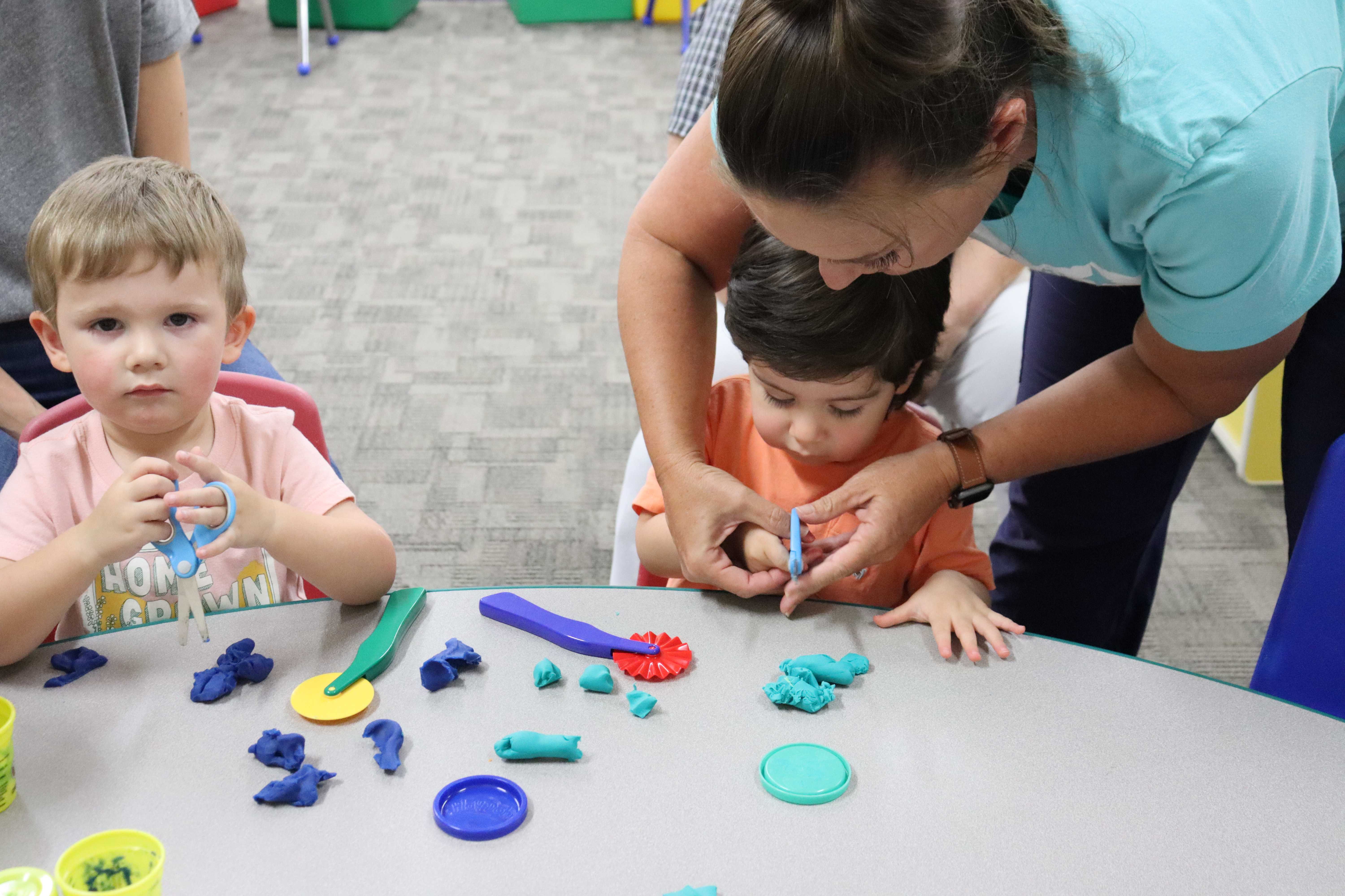 teacher helping child cut playdoh